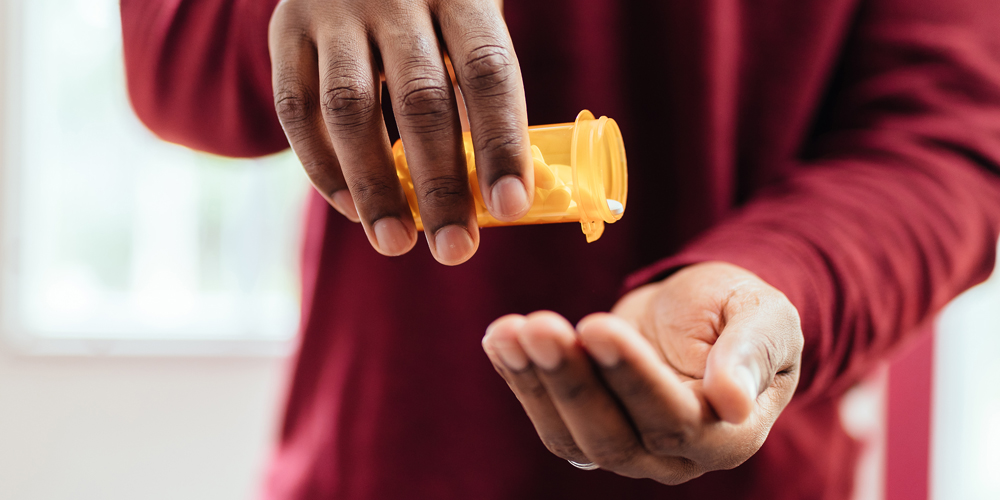 An adult African American male pouring pills from a pill bottle into his hand