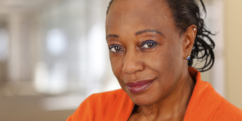 An adult African American female wearing an orange coat and subtly smiling